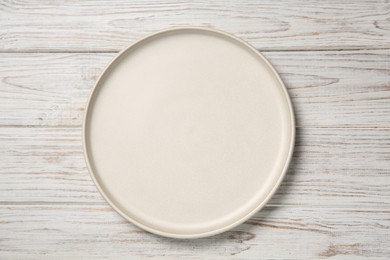 Photo of One white ceramic plate on light wooden table, top view