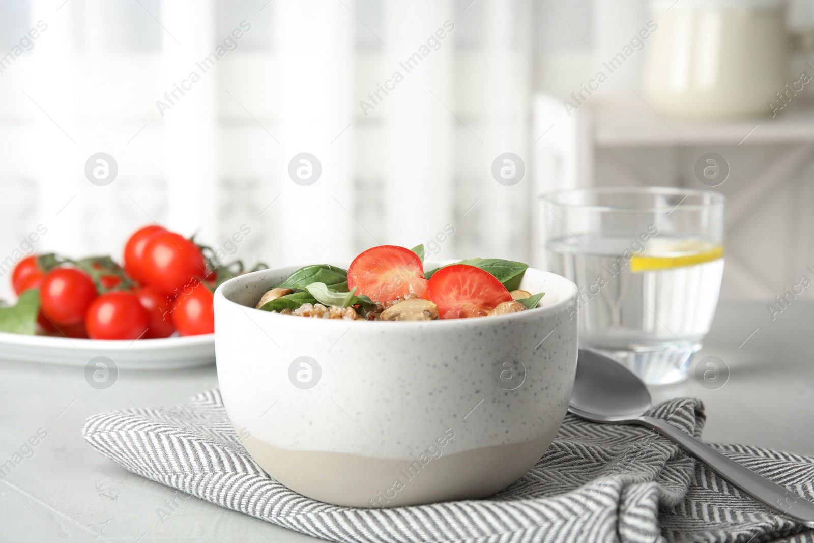 Photo of Delicious buckwheat porridge with mushrooms and tomato on table indoors