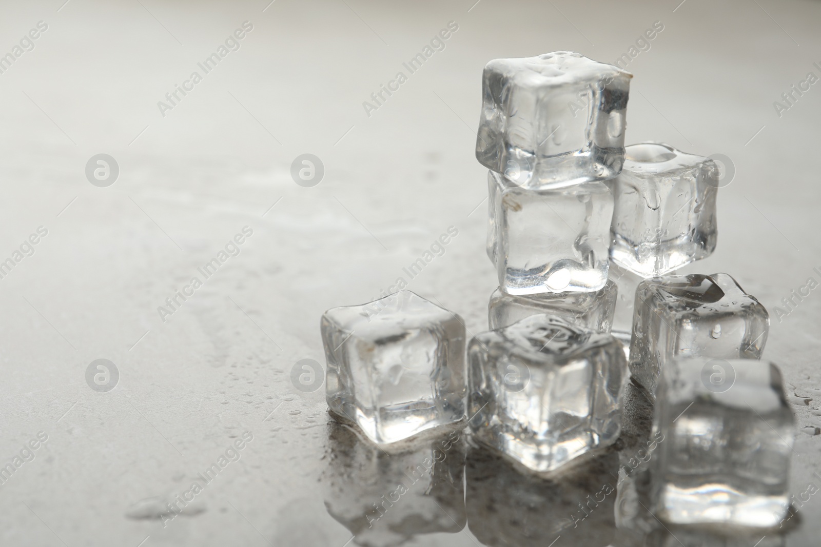 Photo of Crystal clear ice cubes with water drops on grey table, closeup. Space for text