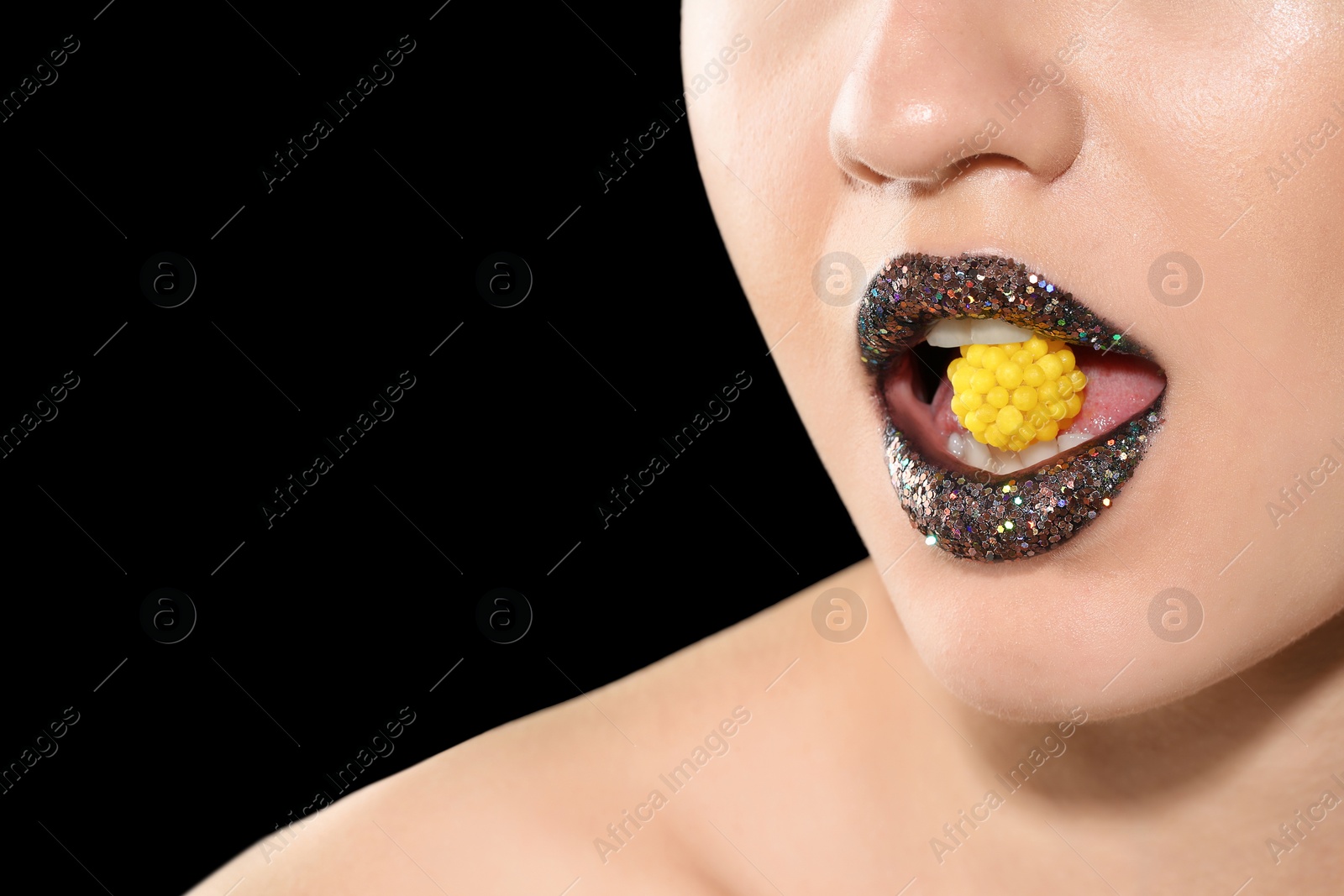 Photo of Beautiful young model with creative makeup holding candy in lips on black background