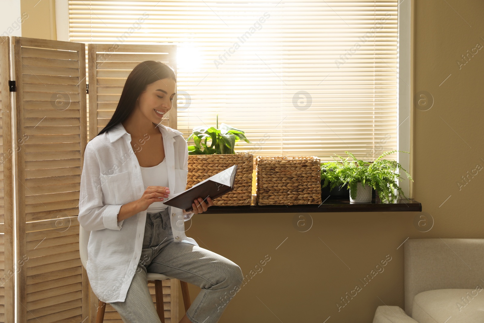 Photo of Beautiful young woman reading book on stool at home