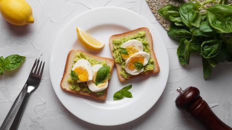 Photo of Tasty sandwiches with boiled egg, avocado and spinach served on white textured table, flat lay