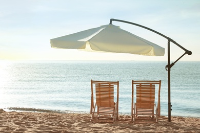 Wooden deck chairs and outdoor umbrella on sandy beach. Summer vacation