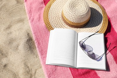 Photo of Open book, sunglasses, hat and striped towel on sandy beach, above view. Space for text