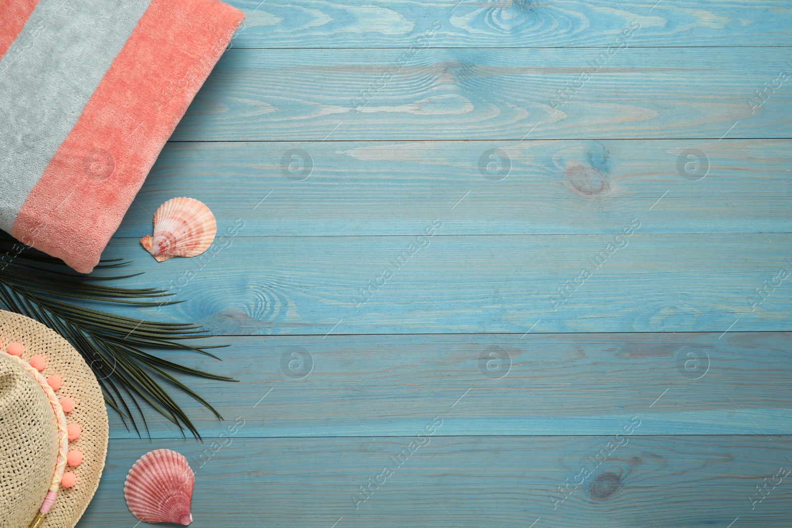 Photo of Beach towel and straw hat on light blue wooden background, flat lay. Space for text