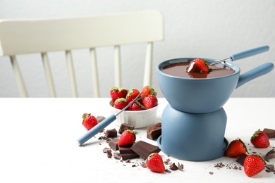 Photo of Fondue pot with chocolate and fresh strawberries on white table. Space for text
