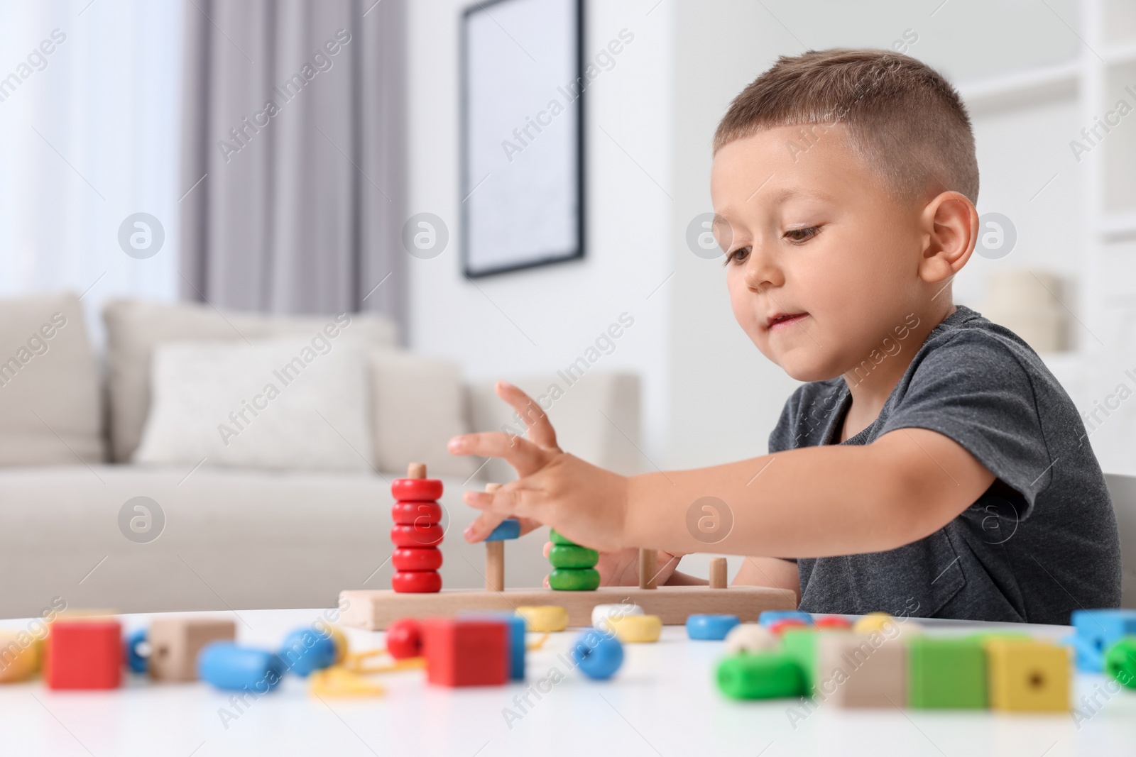 Photo of Motor skills development. Little boy playing with stacking and counting game at table indoors