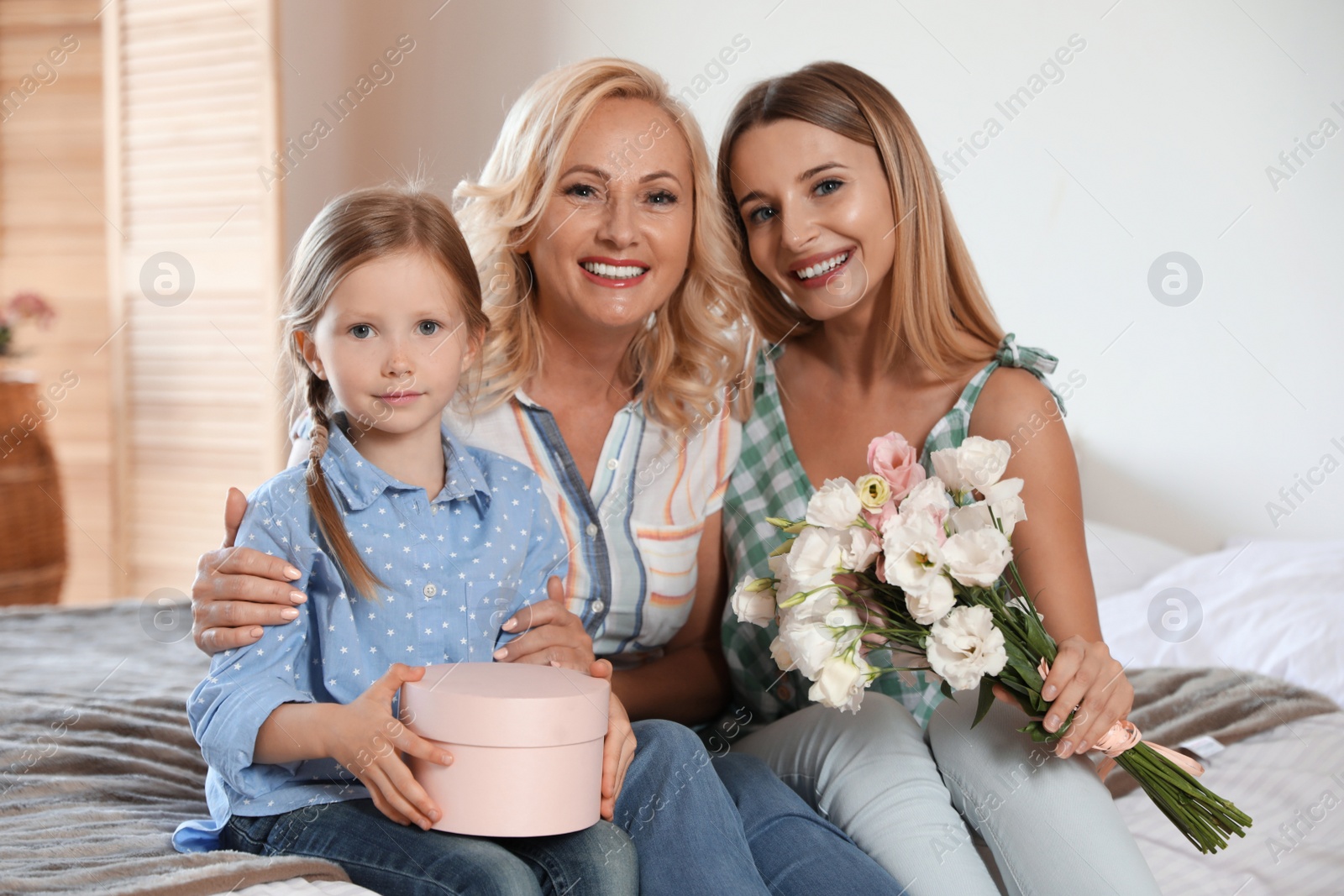 Photo of Young woman with her mature mother and little daughter in bedroom. Holiday celebration