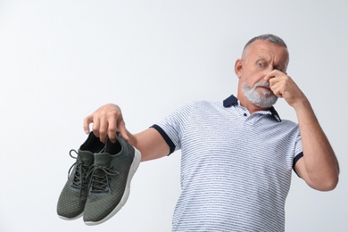 Man feeling bad smell from shoes on white background. Air freshener