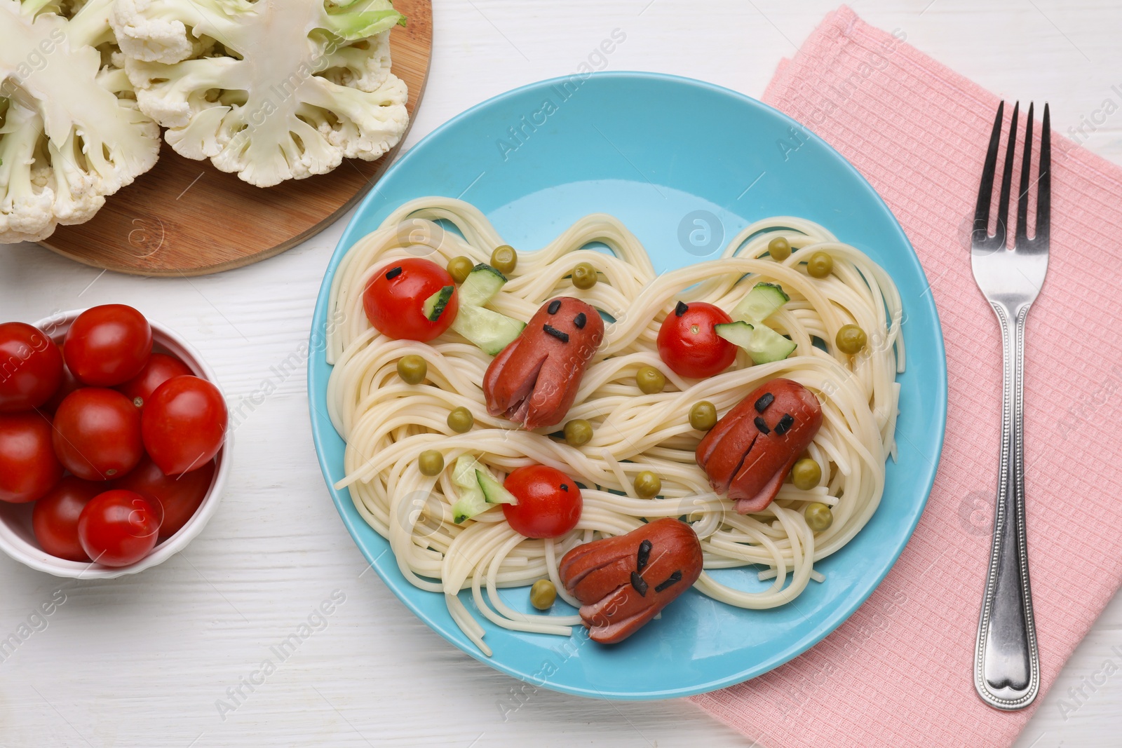 Photo of Creative serving for kids. Plate with cute octopuses made of sausages, pasta and vegetables on white wooden table, flat lay