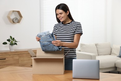 Photo of Young woman with just unpacked new jeans at wooden table indoors. Online shopping