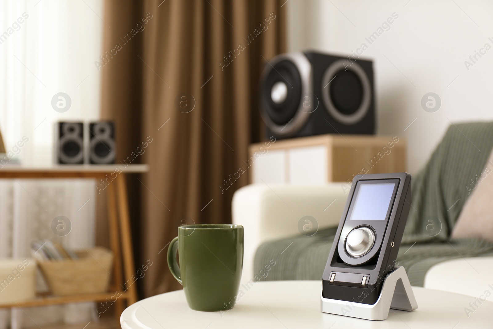 Photo of Remote control of audio speaker system and cup on white table indoors