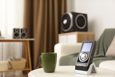 Photo of Remote control of audio speaker system and cup on white table indoors