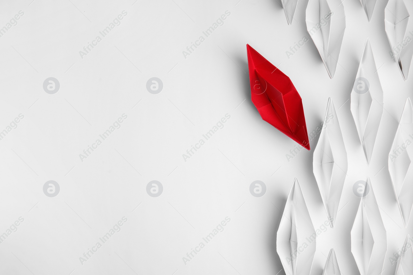 Photo of Red paper boat floating away from others on white background, flat lay with space for text. Uniqueness concept