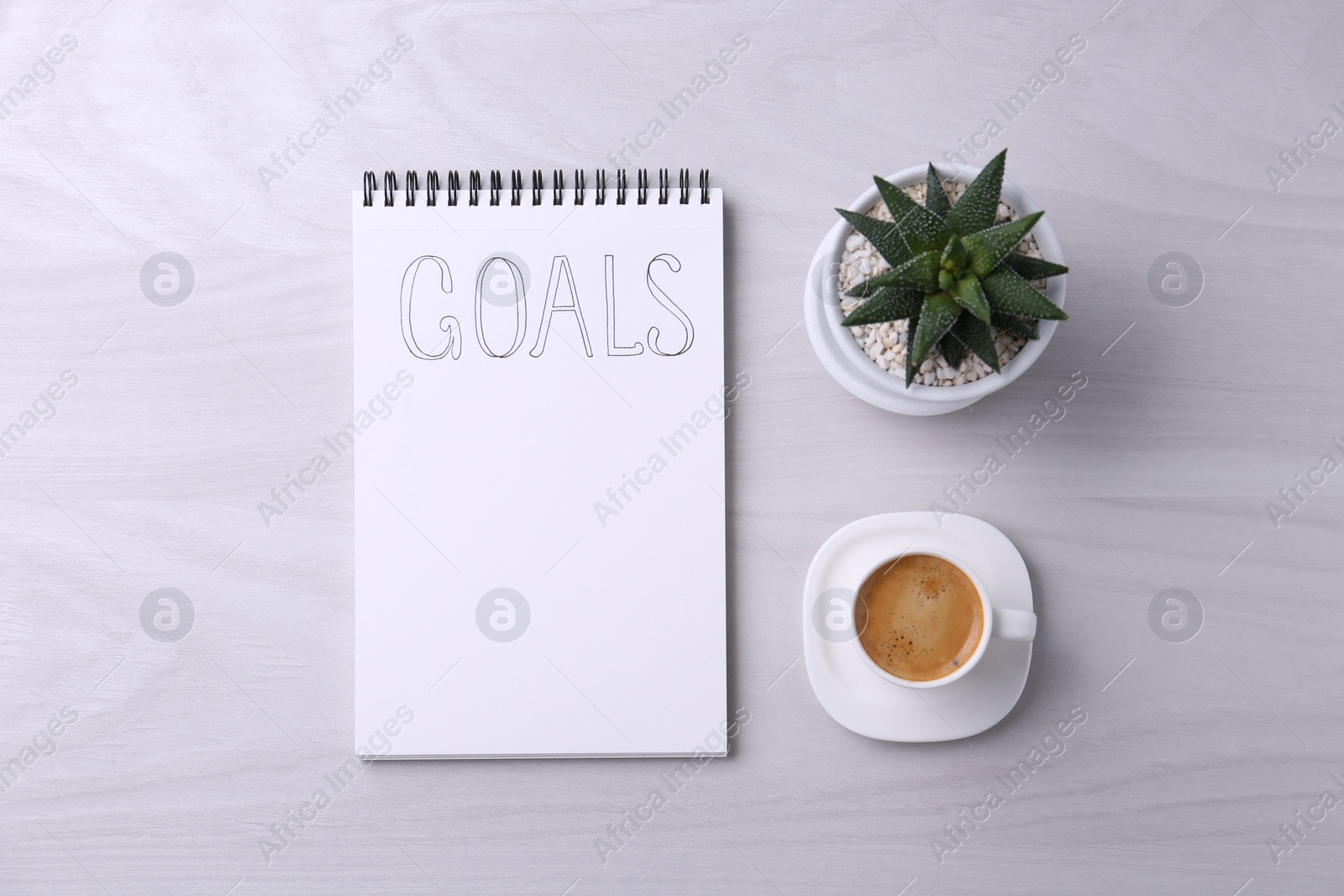 Photo of Notebook with word Goals, houseplant and cup of coffee on white wooden table, flat lay. Planning concept