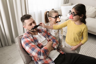 Photo of Cute little children putting fake mustache on father while he sleeping at home
