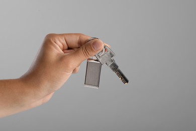 Photo of Woman holding key with metallic keychain on grey background, closeup. Space for text