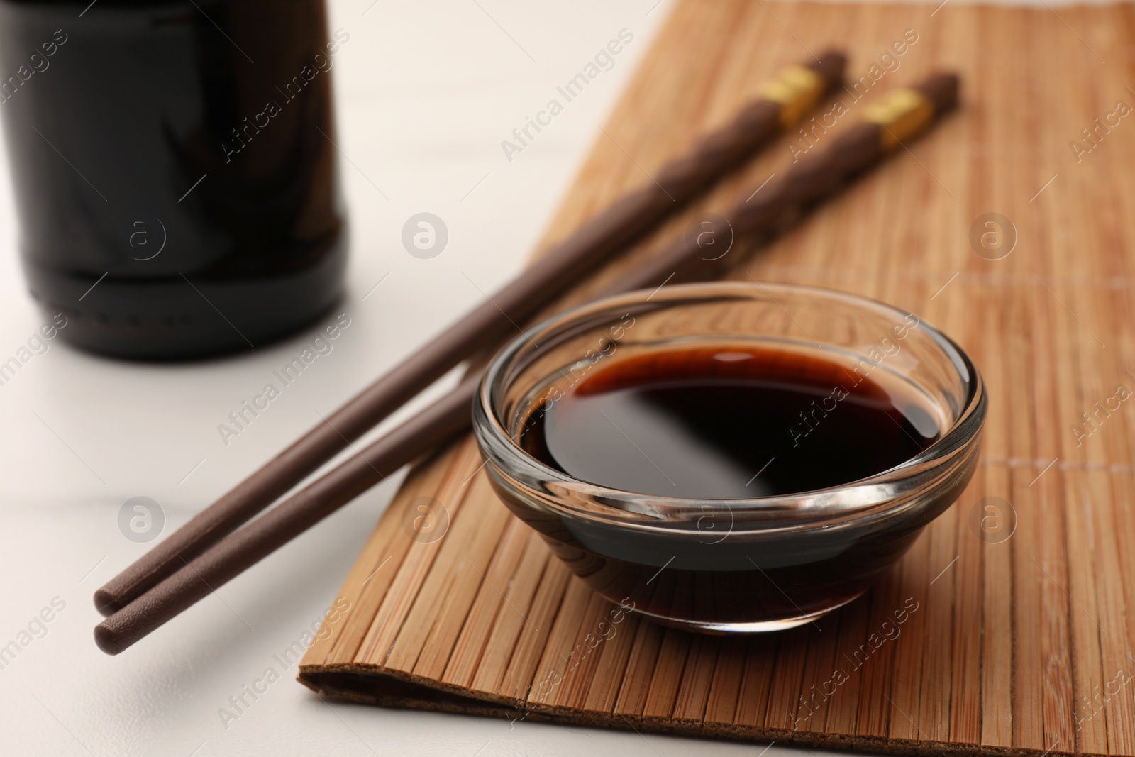 Photo of Bowl with soy sauce and chopsticks on white table, closeup