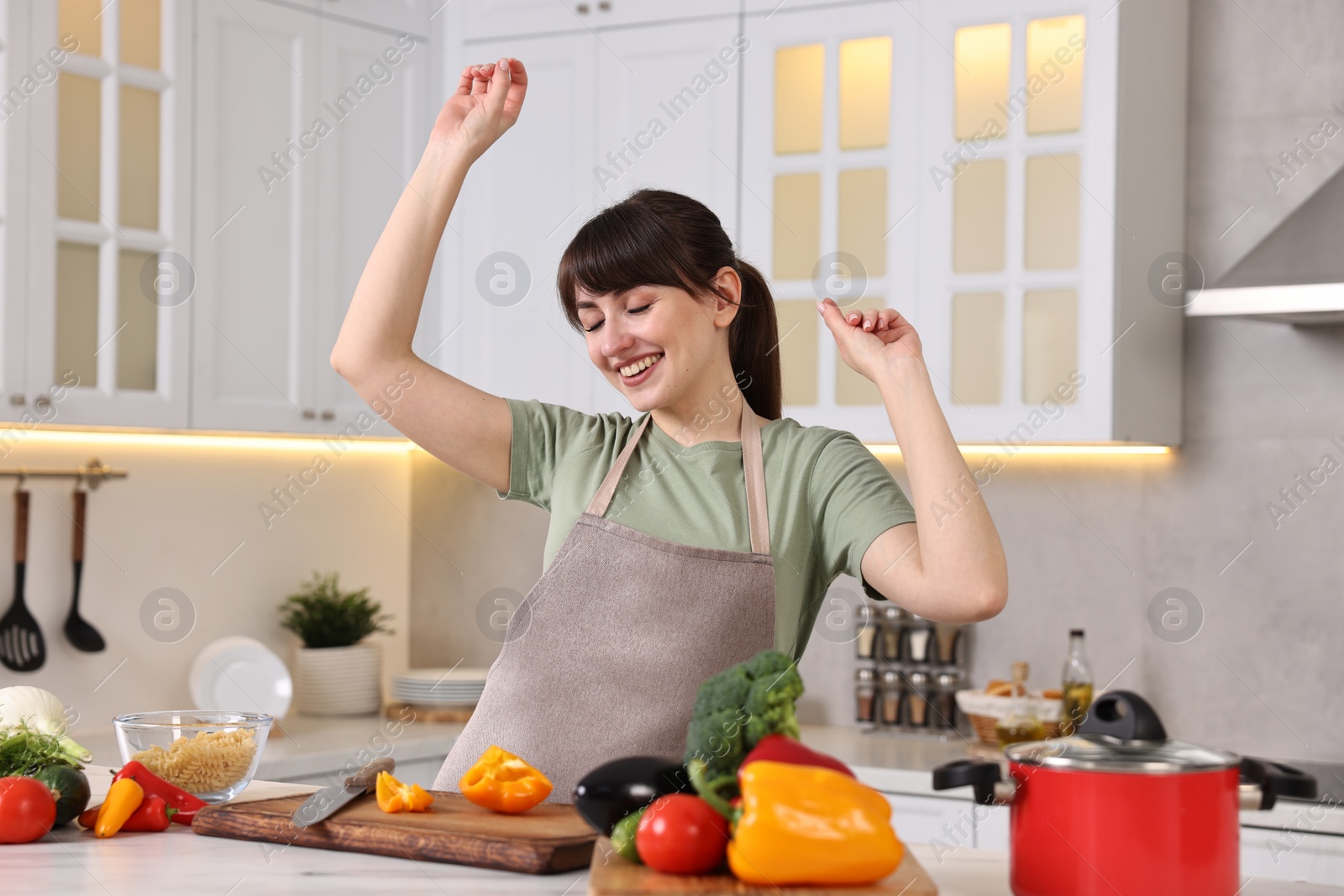 Photo of Happy young housewife having fun while cooking at white marble table in kitchen