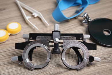 Photo of Trial frame with different ophthalmologist tools on wooden background, closeup