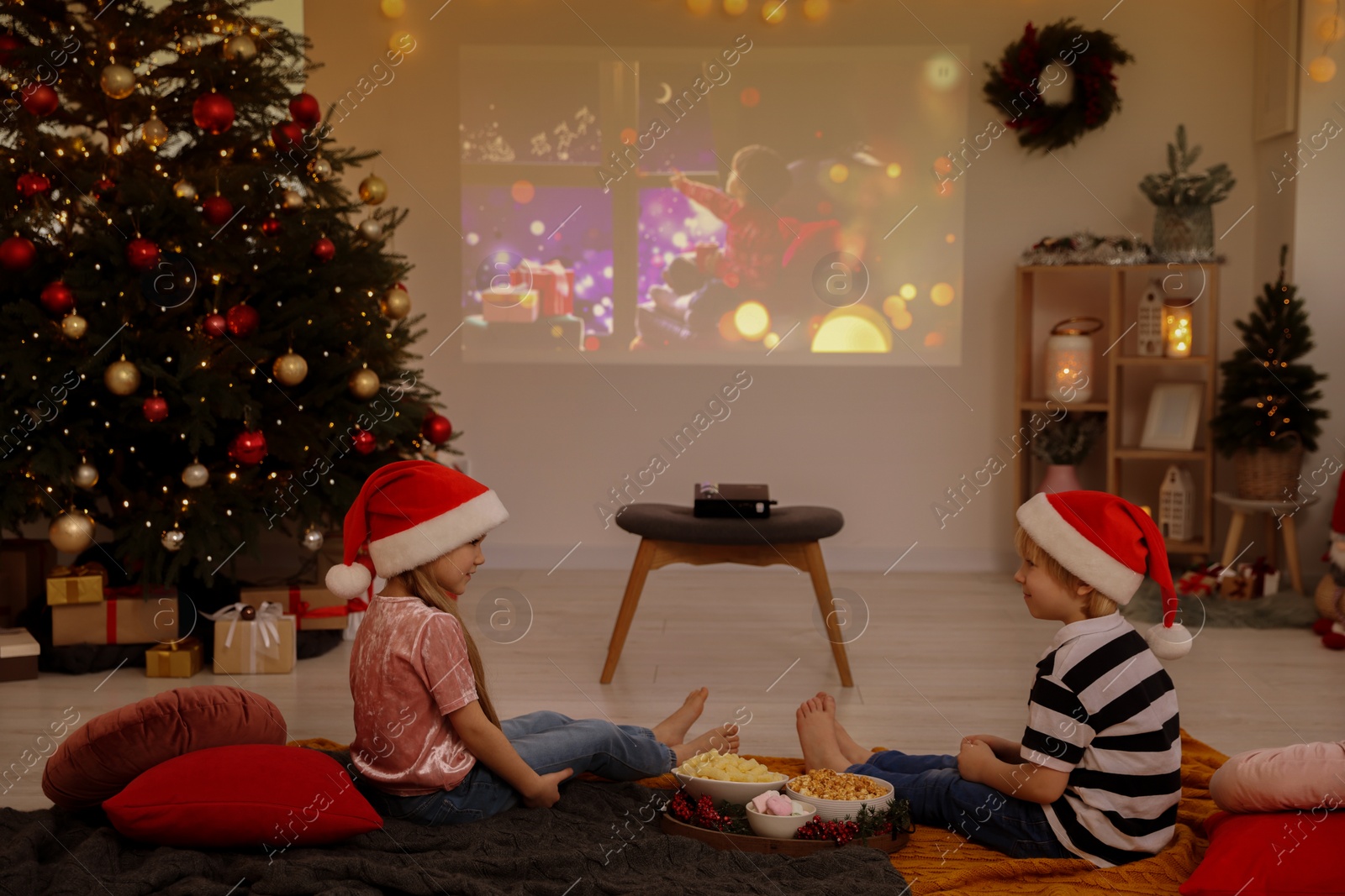 Photo of Brother and sister spending time together near video projector in room. Christmas atmosphere