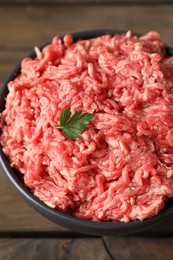 Photo of Raw ground meat and parsley in bowl on wooden table, closeup