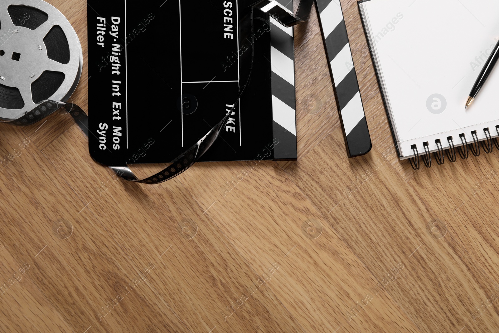 Photo of Movie clapper, film reel, notebook and pen on wooden table, flat lay. Space for text