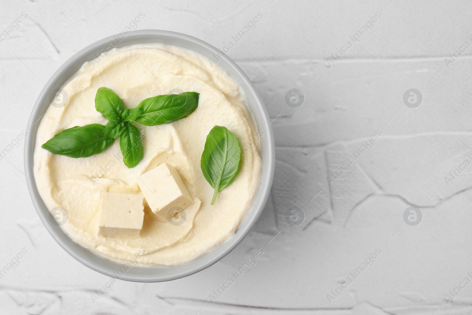 Photo of Delicious tofu sauce and basil leaves on white textured table, top view. Space for text