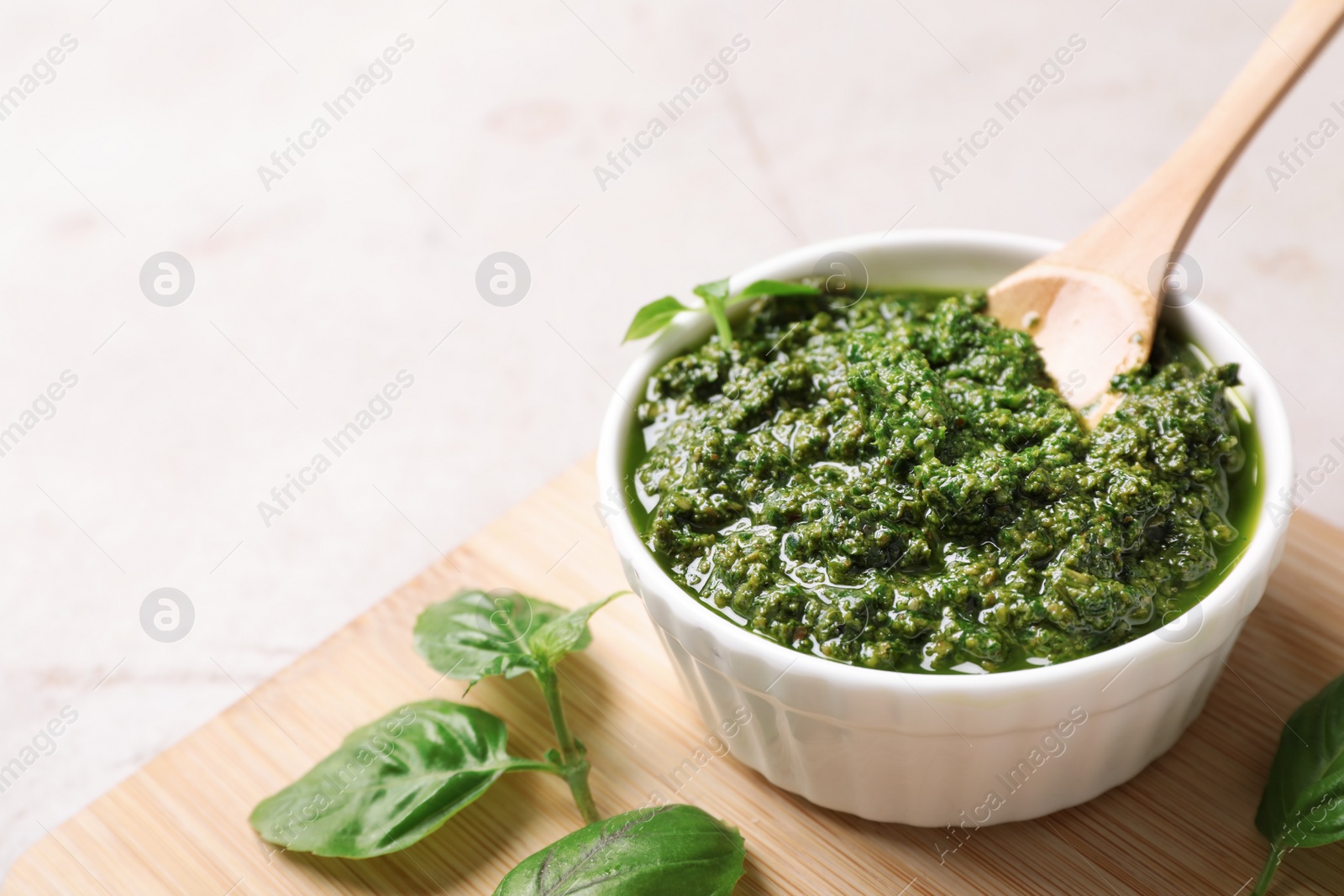 Photo of Board with homemade basil pesto sauce in bowl on table