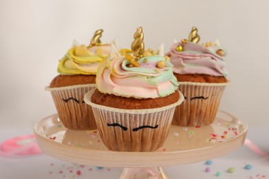 Photo of Dessert stand with cute sweet unicorn cupcakes on white background, closeup