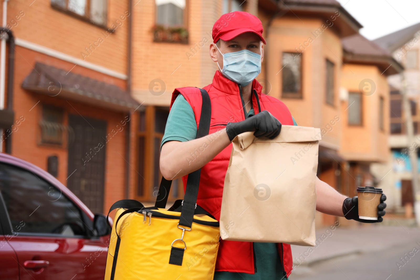 Photo of Courier in protective mask and gloves with orders near car outdoors. Food delivery service during coronavirus quarantine