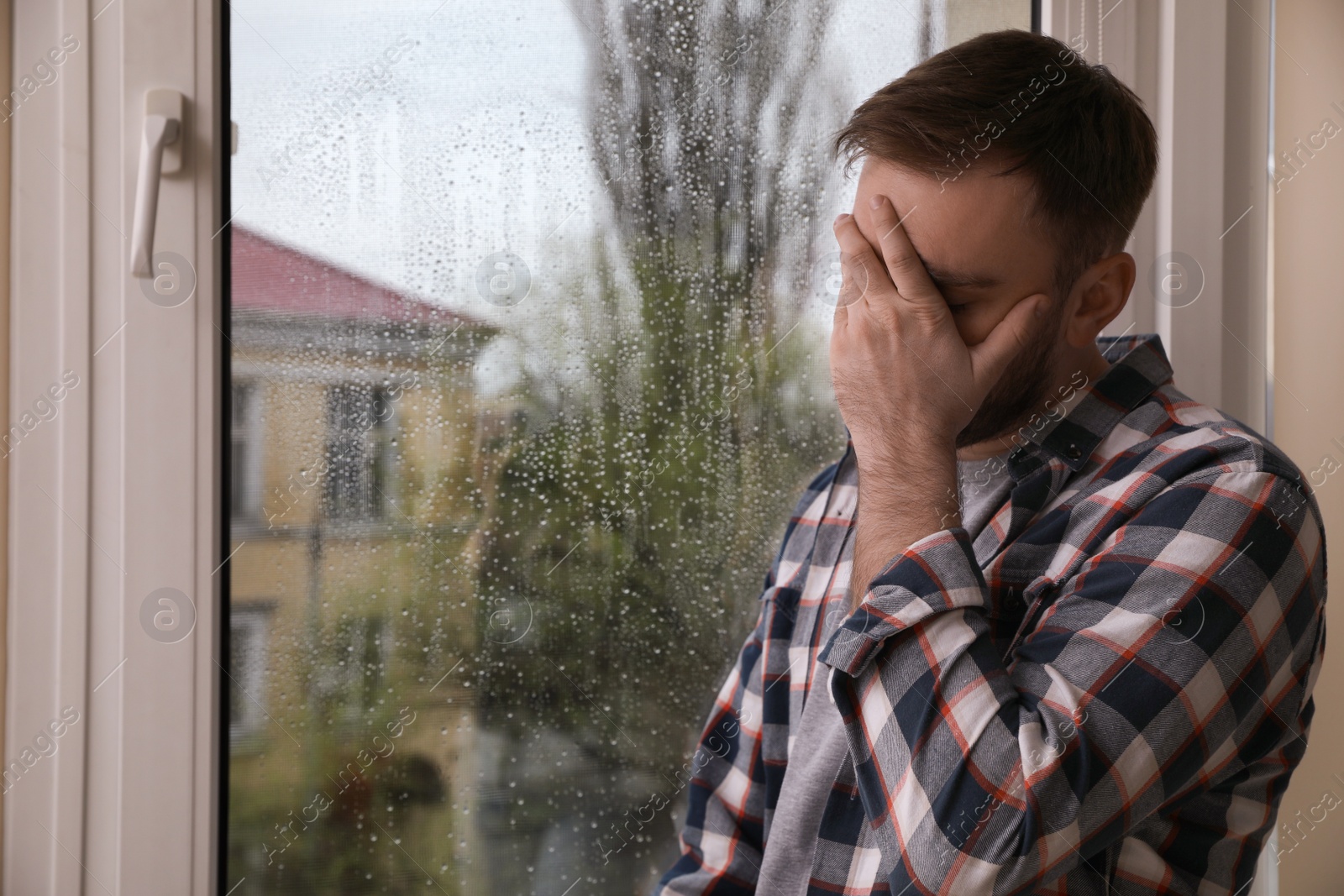 Photo of Depressed man near window at home. Space for text