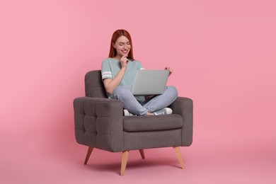 Photo of Smiling young woman with laptop sitting in armchair on pink background