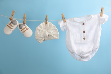 Photo of Baby clothes and accessories hanging on washing line against light blue background