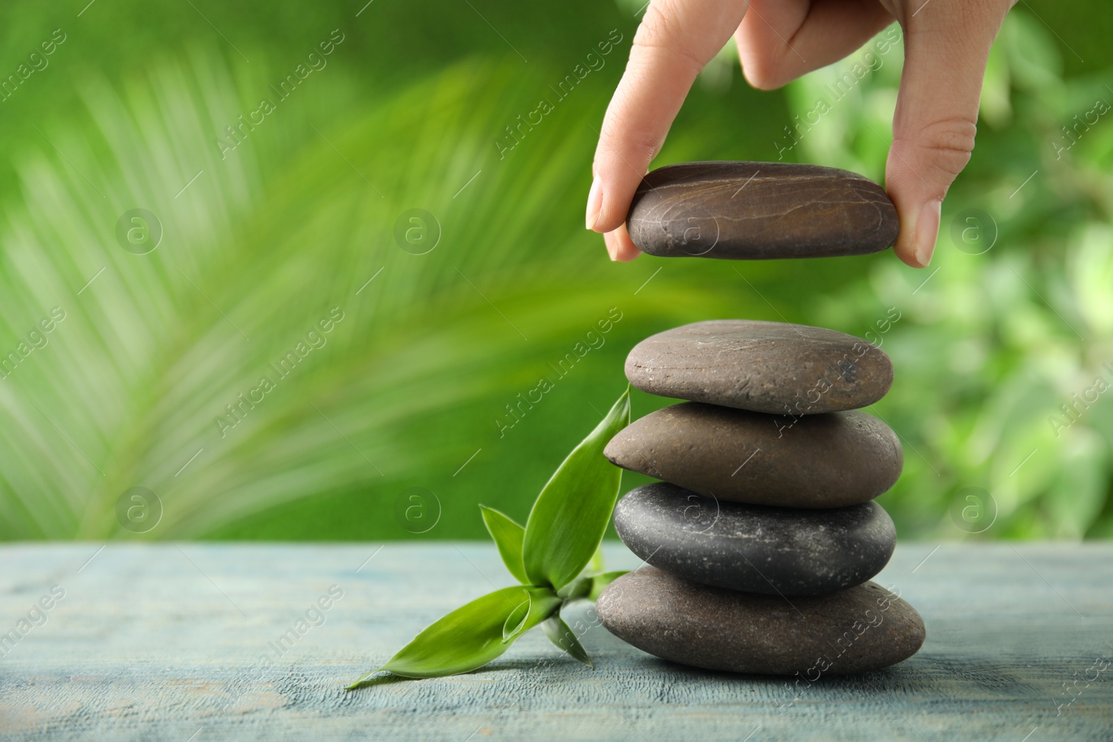 Photo of Woman stacking stones on table against blurred background, closeup. Zen concept