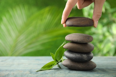 Photo of Woman stacking stones on table against blurred background, closeup. Zen concept