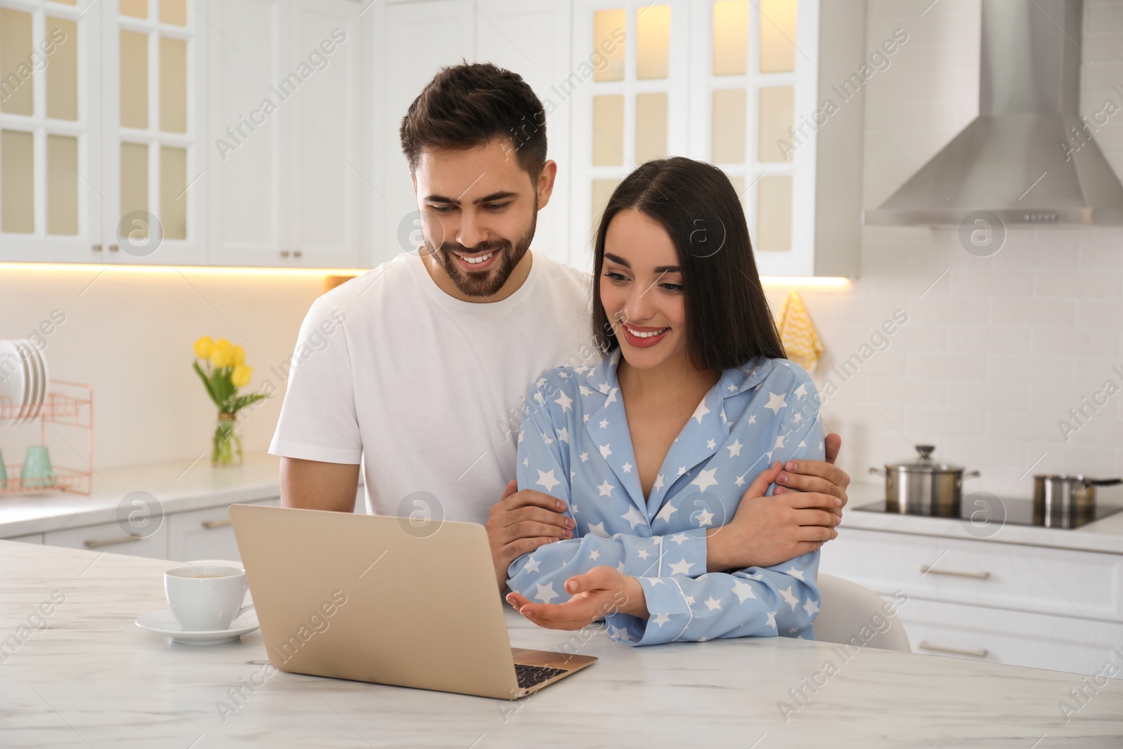 Photo of Happy couple in pajamas with laptop at kitchen table