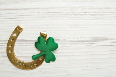 Golden horseshoe and decorative clover leaf on white wooden table, flat lay with space for text. Saint Patrick's Day celebration