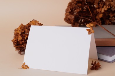Photo of Dried hortensia flowers and sheet of paper on beige table. Space for text