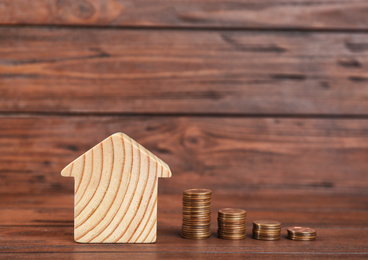 House model and coins on wooden background. Space for text