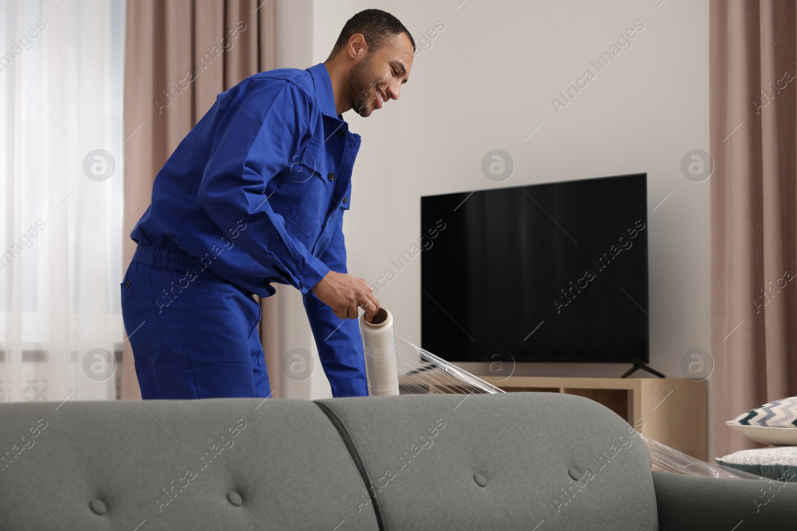 Photo of Male mover with stretch film wrapping sofa in new house