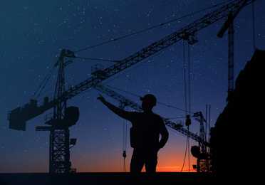 Image of Silhouettes of engineer and construction crane at sunset