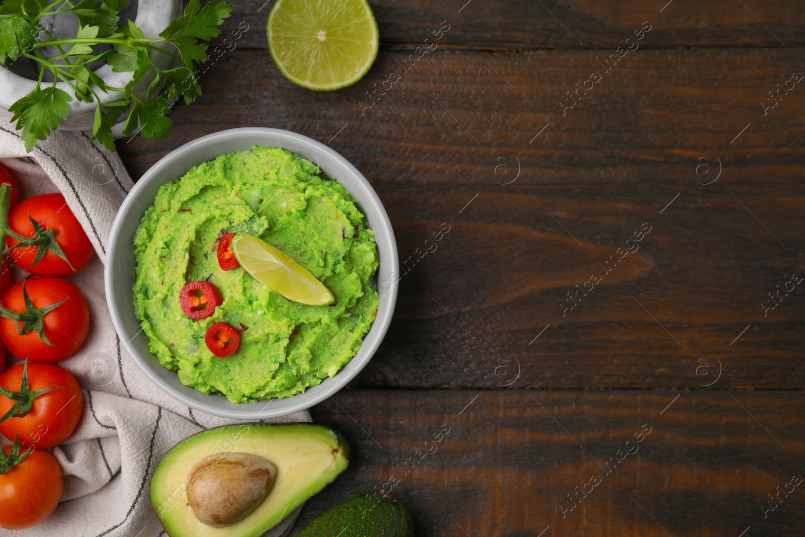 Photo of Bowl of delicious guacamole and ingredients on wooden table, flat lay. Space for text