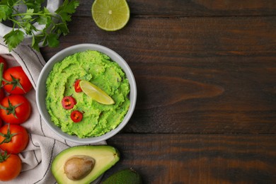 Bowl of delicious guacamole and ingredients on wooden table, flat lay. Space for text