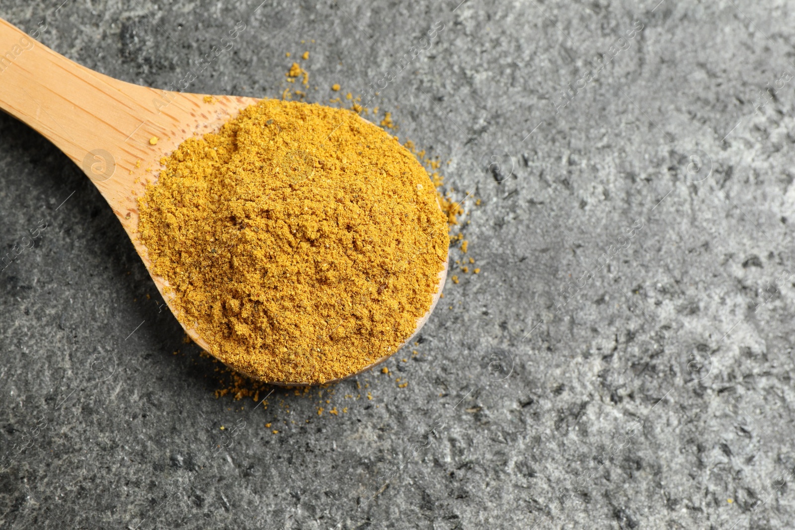 Photo of Spoon with dry curry powder on dark textured table, top view. Space for text