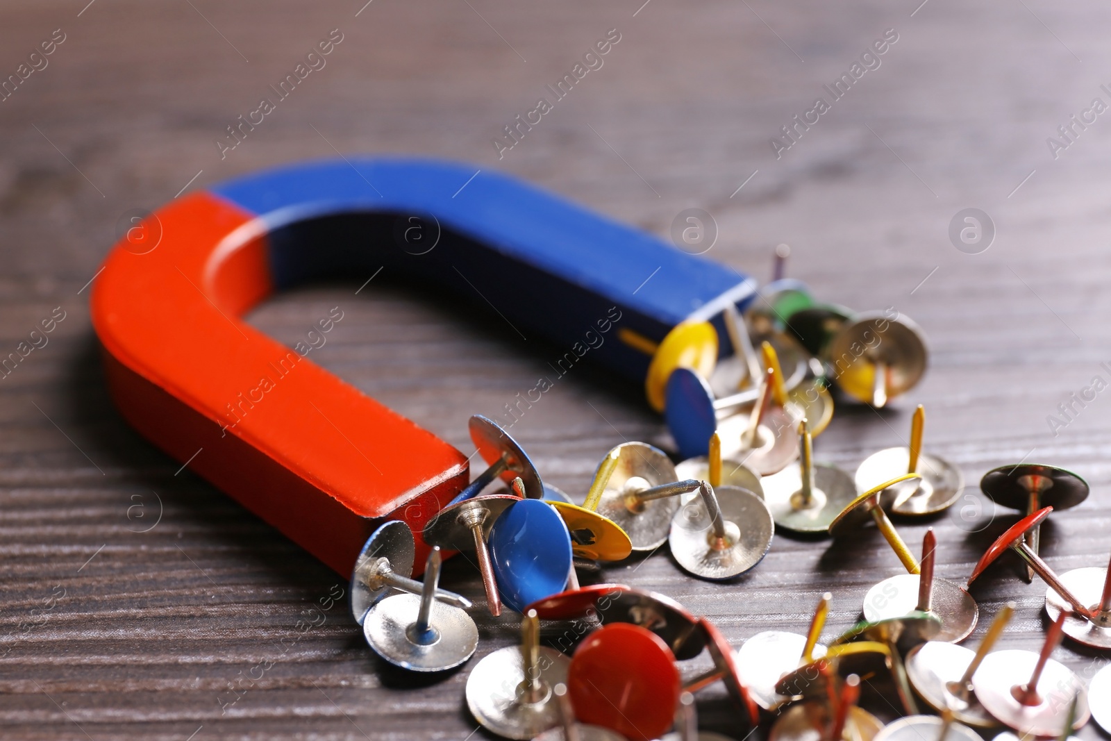 Photo of Magnet attracting colorful drawing pins on dark grey wooden background, closeup