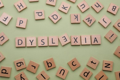 Word Dyslexia with inverted letter E of wooden tiles on olive background, flat lay