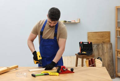 Photo of Young worker using electric drill at table in workshop