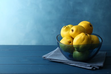 Photo of Tasty ripe quinces in bowl on blue wooden table, space for text