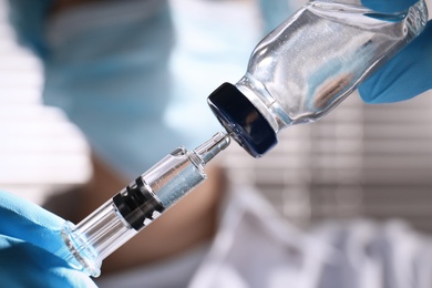 Woman filling syringe with vaccine from vial on blurred background, closeup